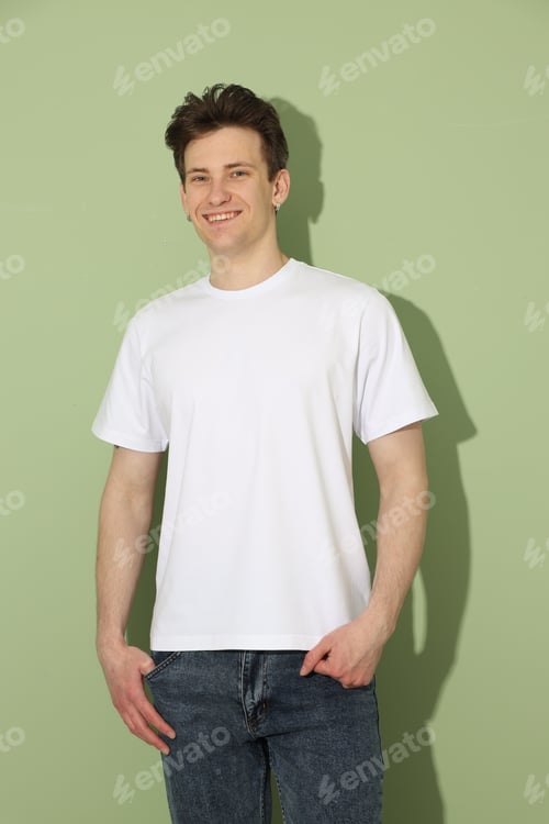 Preview: Handsome young man wearing blank white t-shirt on light green background. Mockup for design