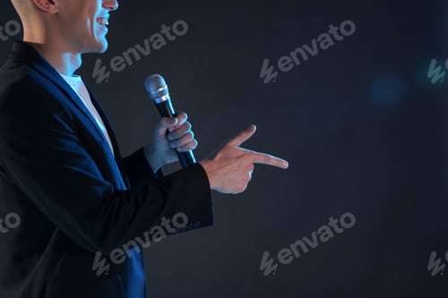 Preview: Happy presenter with microphone performing on dark background, closeup. Space for text