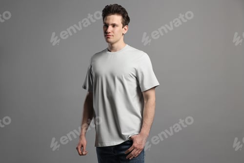 Preview: Handsome young man in blank t-shirt on grey background. Mockup for design