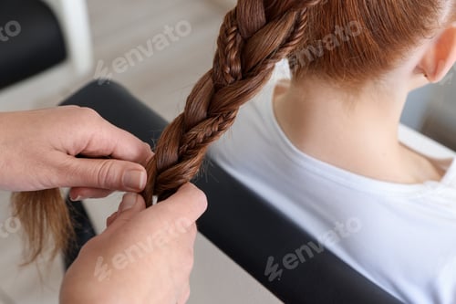 Preview: Hairstylist braiding teenage girl's hair in salon, closeup
