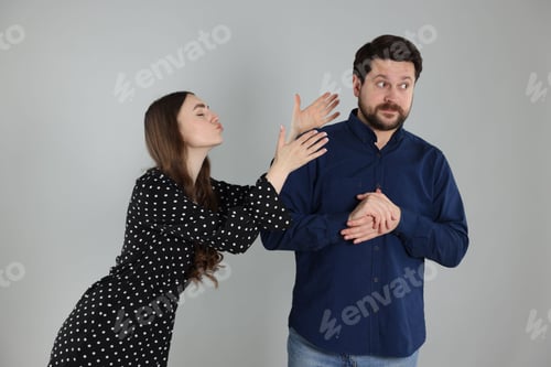 Preview: Embarrassed man refusing kiss from woman on light grey background