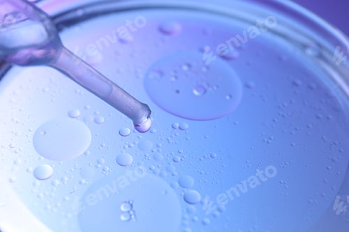 Preview: Dripping liquid from pipette into Petri dish on color background, closeup