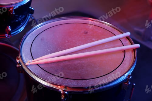 Preview: Wooden drumsticks on drum in color light against dark background, closeup