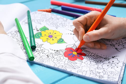 Preview: Woman coloring antistress picture with felt tip pen at light blue wooden table, closeup