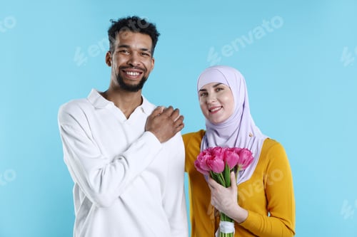 Preview: Portrait of happy muslim couple with beautiful tulips on light blue background