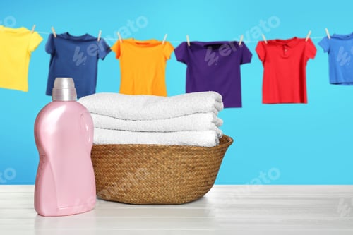 Preview: Laundry basket with clean towels and bottle of detergent on table. Clothes drying against sky