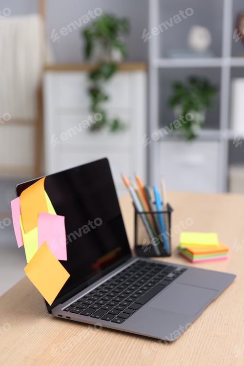 Preview: Laptop with colorful sticky notes and stationery on wooden table indoors. Multitasking, deadline and