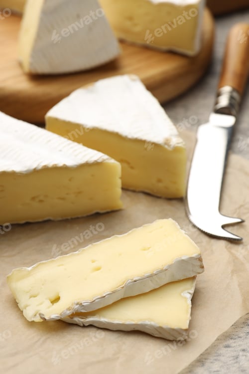Preview: Cut delicious brie cheese and knife on grey table, closeup