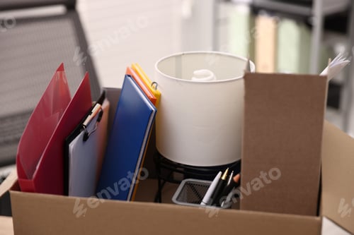 Preview: Dismissal. Different personal belongings in cardboard box on table in office, closeup