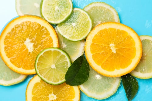 Preview: Citrus slices and green leaves in water on light blue background, flat lay
