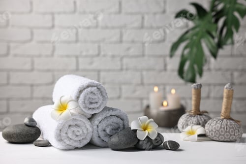 Preview: Terry towels, spa stones, plumeria flowers and herbal bags on white table indoors