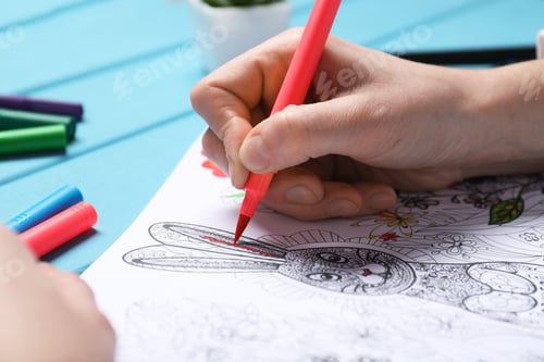 Preview: Woman coloring antistress picture with felt tip pen at light blue wooden table, closeup