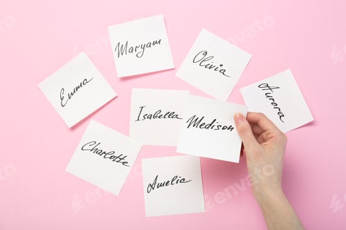 Preview: Woman holding paper stickers with name on pink background, top view. Choosing baby's name