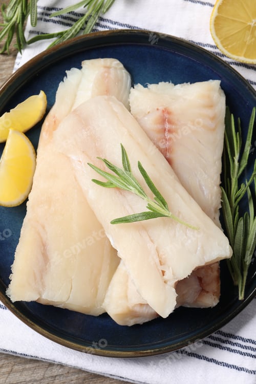 Preview: Pieces of raw cod fish, rosemary and lemon on table, top view