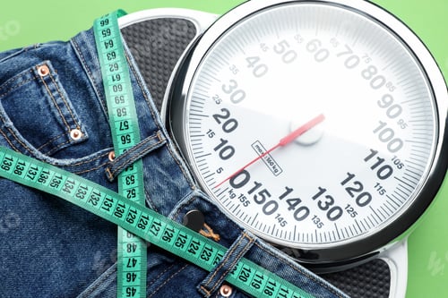 Preview: Jeans with measuring tape and scales on green background, top view