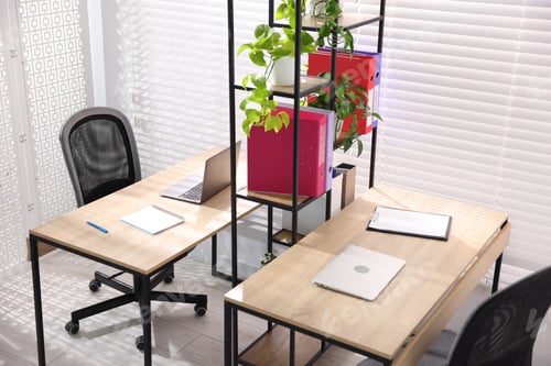Preview: Wooden desks with laptops, chairs, stationery, plants and shelving unit in office. Interior design