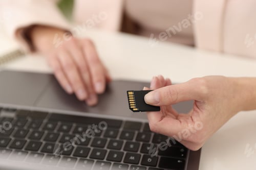 Preview: Woman with SD card working on laptop at desk, closeup