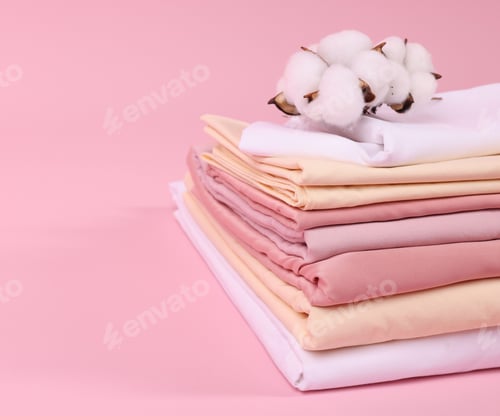 Preview: Stack of fresh bed linens and cotton flowers on pink background, closeup. Space for text