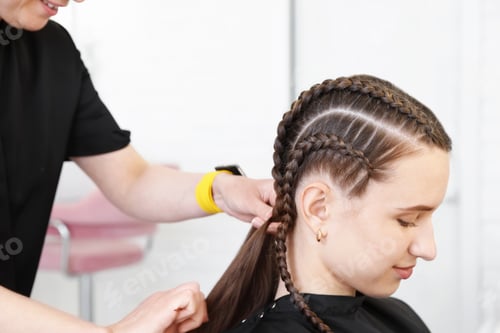 Preview: Hairstylist braiding teenage girl's hair in salon, closeup