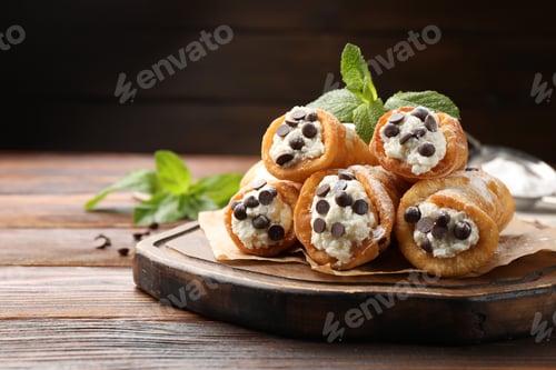 Preview: Delicious cannoli with cheese, chocolate chips, powdered sugar and mint on wooden table, closeup. Sp