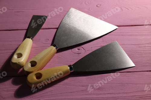 Preview: Putty knives on pink wooden table, closeup. Construction tool