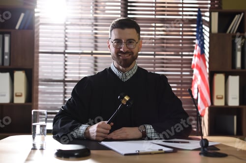 Preview: Portrait of smiling judge in glasses with gavel at table in office