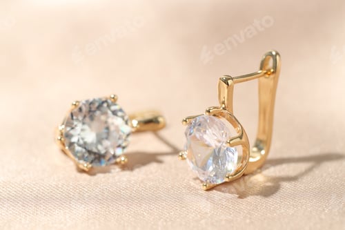 Preview: Pair of golden earrings on beige fabric, closeup