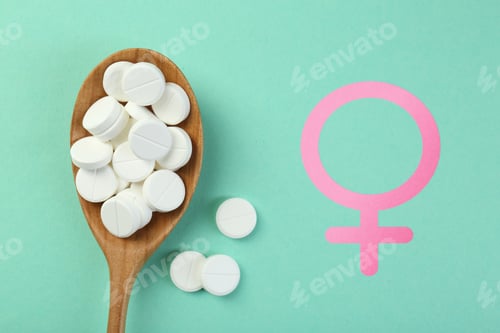 Preview: Female hormones. Spoon with pills and female gender symbol on turquoise background, top view