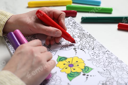 Preview: Woman coloring antistress picture with felt tip pen at white table, closeup