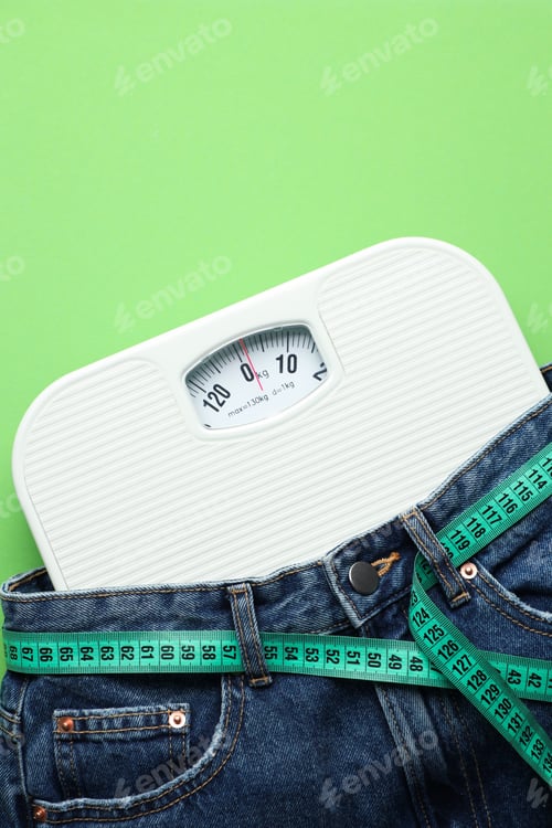 Preview: Jeans with measuring tape and scales on green background, top view. Space for text