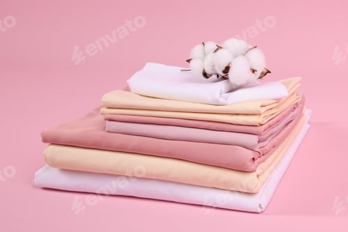 Preview: Stack of fresh bed linens and cotton flowers on pink background, closeup