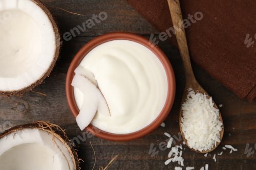 Preview: Delicious coconut yogurt in bowl, flakes and halves of fruit on wooden table, flat lay