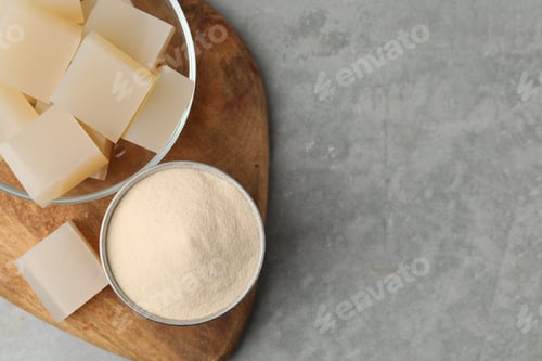 Preview: Gelatin powder and jelly cubes in bowl on gray textured table, top view. Space for text