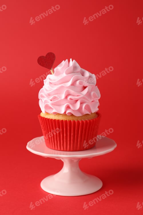 Preview: Happy Valentine's Day. Tasty cupcake with heart topper on red background, closeup