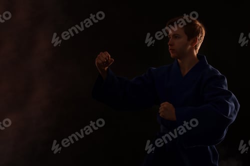 Preview: Man in uniform practicing karate on black background with smoke, space for text