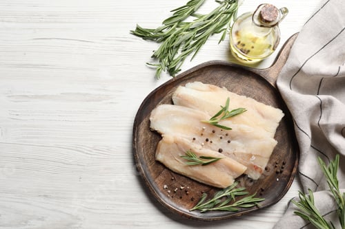 Preview: Raw cod fish, rosemary, oil and spices on white wooden table, flat lay. Space for text