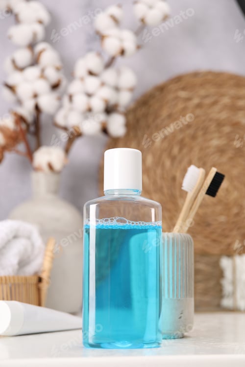Preview: Bottle of mouthwash and toothbrushes on white table in bathroom