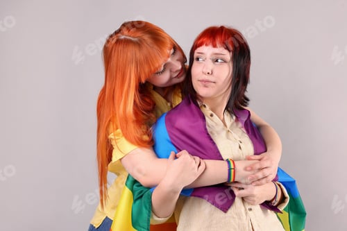 Preview: Lovely lesbian couple with rainbow flag on gray background. LGBT concept