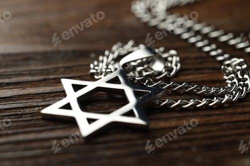 Preview: Holocaust Remembrance Day. Pendant in shape of Star of David and metal chain on wooden table, closeu