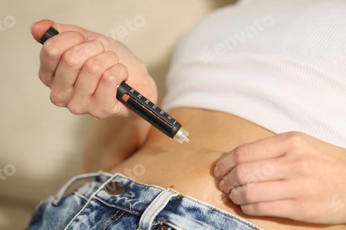 Preview: Diabetes. Woman making insulin injection into her belly with autoinjector indoors, closeup