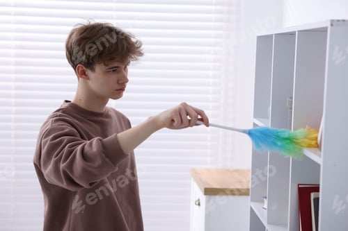 Preview: Housework. Teenage boy removing dust from shelf with static duster at home