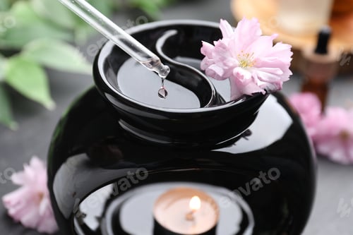 Preview: Aromatherapy. Dripping essential oil into aroma lamp on black table, closeup