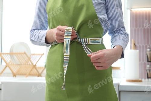 Preview: Woman tying clean apron at home, closeup