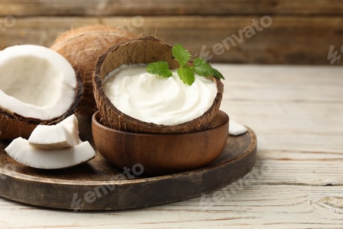 Preview: Tasty coconut yogurt with melissa leaves in shell and nuts on white wooden table, closeup. Space for