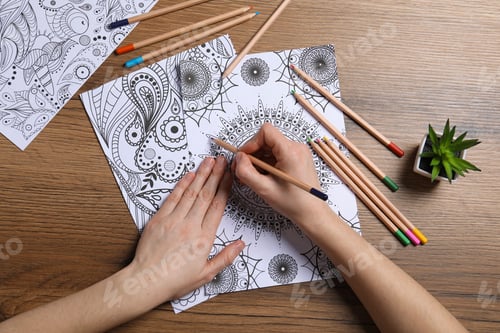 Preview: Woman coloring antistress picture with pencils at wooden table, top view