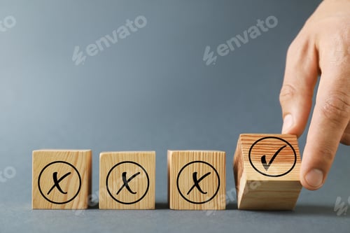 Preview: Man putting wooden cube with checkmark next to others with cross marks on grey background, closeup.