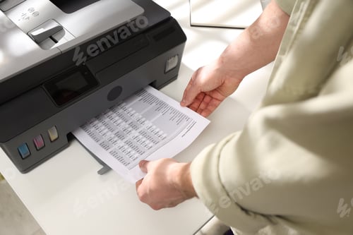 Preview: Man taking printed sheet of paper from printer at white desk indoors, above view