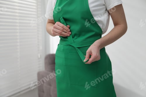 Preview: Woman tying clean apron at home, closeup. Space for text