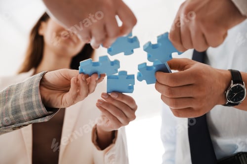 Preview: Team building. Group of businesspeople putting puzzle pieces together indoors, low angle view