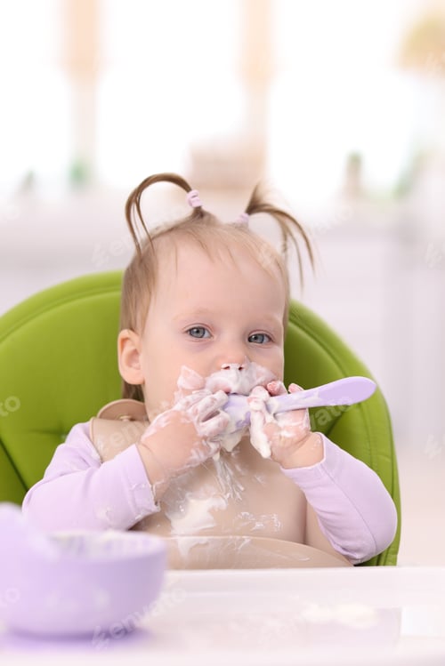 Preview: Cute little child eating baby food on feeding chair at home